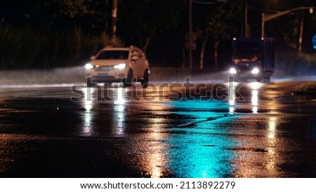 Rainy night in city, cars driving on wet road, rain was illuminated by the headlights of cars, focused on the asphalt road.