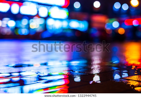 Rainy night in\
the city. Parking mall with cars. Reflections of shop windows on\
the wet pavement. Colorful colors. Close up view from the level of\
the puddle on the\
pavement.
