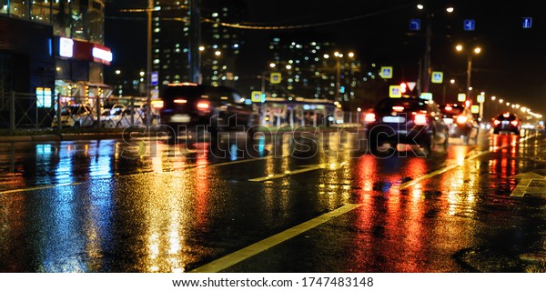 Rainy night in the city. Wet street,\
cars, colored lights reflection and blurred\
silhouettes