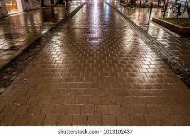 Rainy night over a pedestrian street with cobblestone paving and lights reflection from the nearby buildings and street illumination. Bicycles are waiting parked on the side. - Powered by Shutterstock