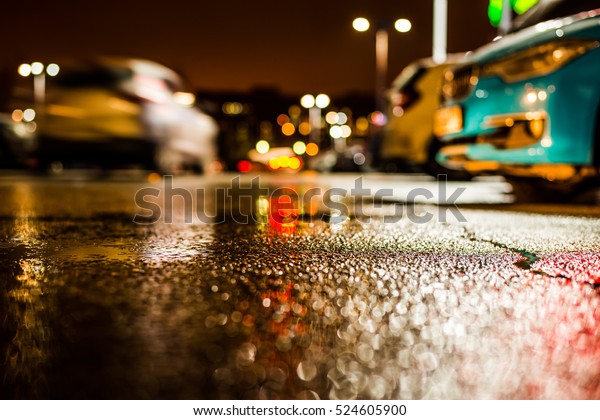 Rainy night in the parking\
shopping mall, the riding car. Close up view from the asphalt\
level