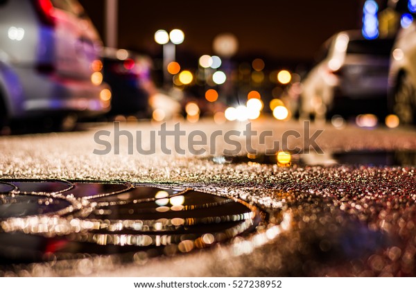Rainy night\
in the parking shopping mall, rows of parked cars. Close up view of\
a hatch at the level of the\
asphalt