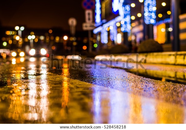 Rainy night in the parking shopping mall, the\
headlights of the approaching cars. Close up view from the level of\
the dividing line