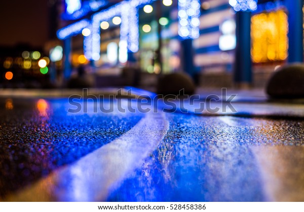 Rainy night in the\
parking shopping mall, illumination lights are reflected in a\
asphalt. Close up view from the level of the dividing line, image\
in the blue tones