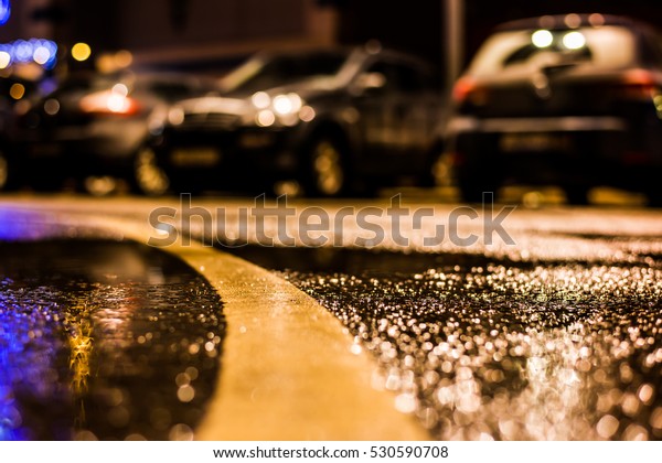 Rainy night in\
the parking shopping mall, rows of parked cars. Close up view from\
the level of the dividing\
line