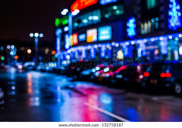 Rainy night in the parking\
shopping mall, rows of parked cars. Defocused image, image in the\
blue tones
