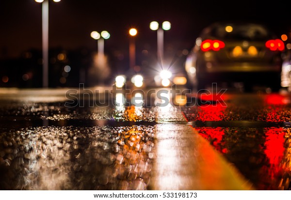 Rainy\
night in the parking shopping mall, the headlights of the cars.\
Close up view from the level of the dividing\
line