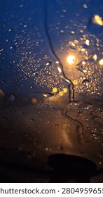 Rainy Night Window Description: Abstract view of rain water droplets on window glass, capturing golden bokeh city lights against a deep navy blue twilight. A moody and atmospheric wallpaper perfect for aesthetic design projects.