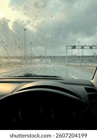 Rainy Road View: A driver's perspective of a rainy day through a car windshield with raindrops.
