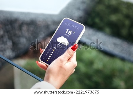 rainy weather. weather forecast for autumn. female hand holds a mobile phone and looks at the weather forecast for the day on a park with a trees background