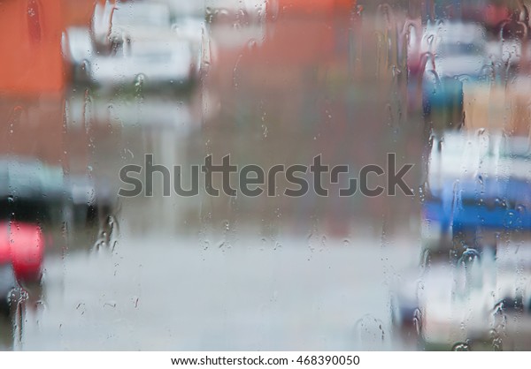 Rainy weather.\
Raindrops flow on window glass and dripping down.  Parking is\
barely visible through the rainy\
mist