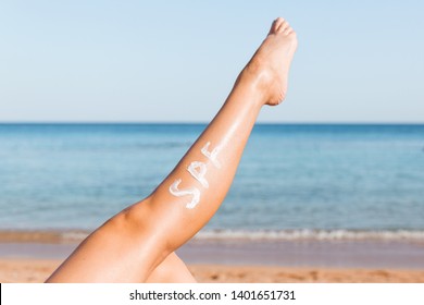Raised up female leg with spf word made of sun cream at the beach. Sun protection factor concept.