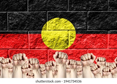 Raised Fists Against The Background Of The Depicted Flag Of Australian Aboriginal On A Brick Wall, A Concept Of Strength And Unity.