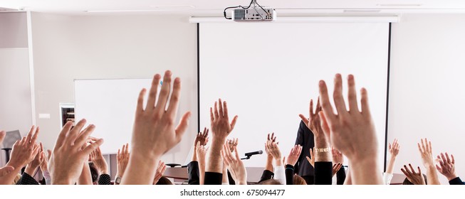 Raised hands and arms of large group of people in class room, audience voting in professional education surrounding, selective focus with anonymous people.
