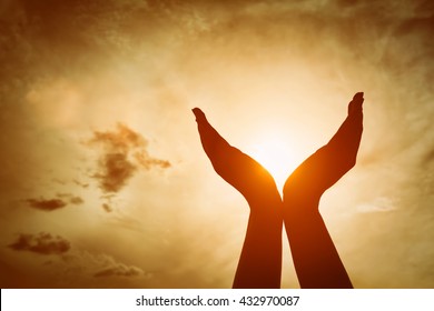 Raised hands catching sun on sunset sky. Concept of spirituality, wellbeing, positive energy etc.