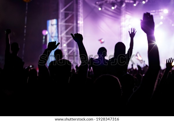 Raised hands in honor of a musical show on stage,\
People in the hall