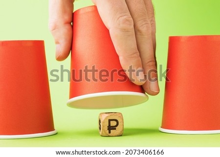 Raised paper cup and wooden cube with Russian ruble symbol underneath, thimble gambling concept