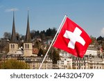 Raised Swiss national flag in front of the two towers of St. Leodegar