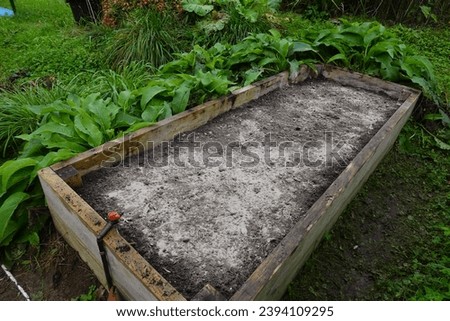 raised wooden bed with a pile of ash to be used as fertilizer and to protect it from pests.