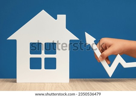 Raising mortgage interest rates. Increasing the bank's margin when buying real estate. A white house symbol with a graph arrow pointing up, on a blue background, close-up. Copy space.