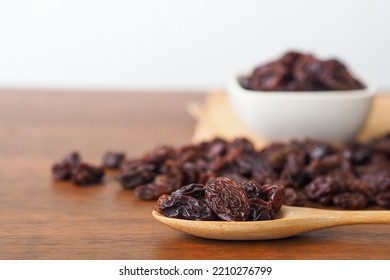 Raisins in wooden spoon on wooden table background. Raisins in white bowl. Dry raisins. Selective focus.