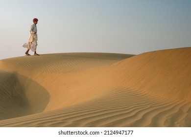 Rajasthan India February 2020: A Nomadic Camel Herder Goes For A Walk As The Sun Sets In The Thar Desert 