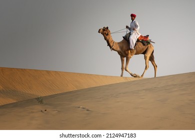 Rajasthan India February 2020: A Nomadic Camel Herder Rides In The Early Morning Light In The Thar Desert