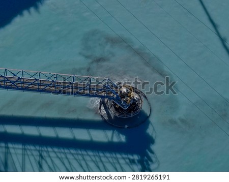 Rake bridge of a thickener rotating over turquoise water at a mineral processing plant