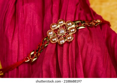 Rakhi On Pink Fabric Background. Golden Gold Plated Wristband Rakhi On Rakshabandhan On Fabric Pink Beight Background For Brother-sister Bond Festival Raksha Bandhan