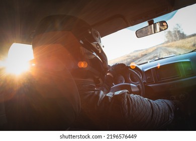 Rally car driver sitting by the steering wheel in the sunset rays concept. - Shutterstock ID 2196576449