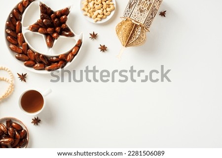Ramadan concept. Crescent and star plate with dried dates, islamic lantern, cup of tea, nuts, rosary breads on white background.