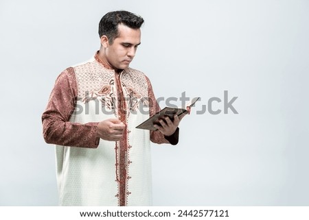 Ramadan, EIDMUBARAK, Portrait Asian Muslim man standing and reading the Quran and appreciates, The Holy Al Quran with written Arabic calligraphy meaning of Al Quran, on white background, copy space.