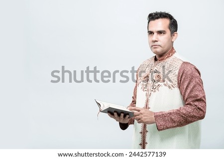 Ramadan, EIDMUBARAK, Portrait Asian Muslim man standing and reading the Quran and appreciates, The Holy Al Quran with written Arabic calligraphy meaning of Al Quran, on white background, copy space.