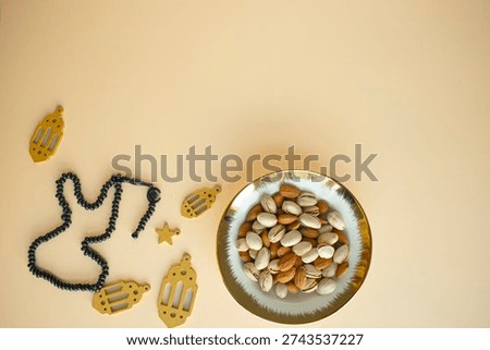 Ramadan flat lay with lantern props, misbaha (prayer beads), and pistachios with almonds arranged on a cream beige background.