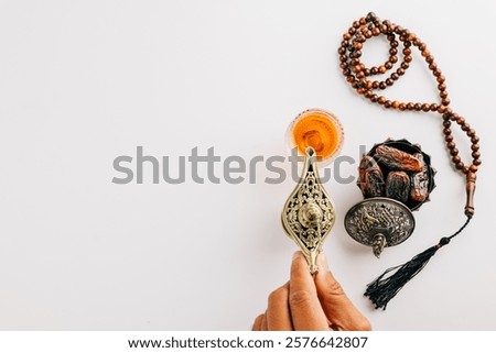Ramadan flat lay with tea, dates, and prayer beads on a white background. A hand pours tea from a teapot, embodying holy traditions and a serene celebration. Ramadan day