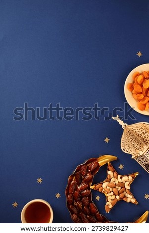Ramadan Iftar flat lay with dates, nuts, apricots and lantern on dark blue background.