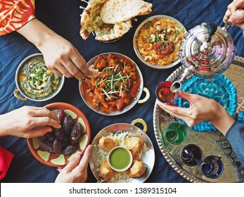 Ramadan Iftar Meal Theme People Eating Variety Foods Together On Dining Table With Large Dates (Medjool), Samosas, Aloo Gobi, Chicken Biryani, Moroccan Tea Set, Palak Paneer And Naan Bread. (top View)