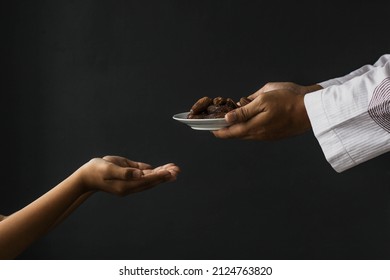 Ramadan kareem concept. Side view Muslim hands giving plate of dates isolated on black background