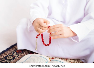 Ramadan Portrait - Hand of Muslim kid making zikr using rosary (praying to Allah) and reading Quran (Holy Muslims Book) 