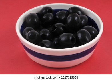 Ramekin Of Pitted Black Olives In A Ramekin Close-up On A Red Background 