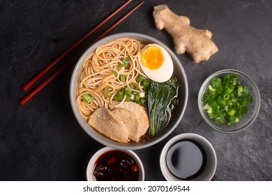 Ramen is asian noodles in a bowl with meat and vegetables or seafood, often flavored with soy sauce or miso, dark background, top view