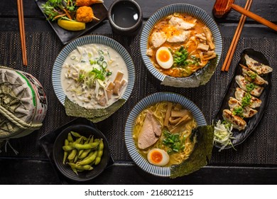 Ramen combo platter with Pork tonkotsu chashu ramen, soy ramen, crab claw, edamame soybeans, spicy fried pork gyoza dumplings on black table, Top view