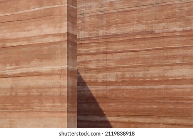 Rammed earth wall, clay old brown-orange background. Surface fine-grain grunge dirty. Natural raw materials mixed soil, gravel, sand, lime, or cement compacted stripe layers natural earth tones autumn