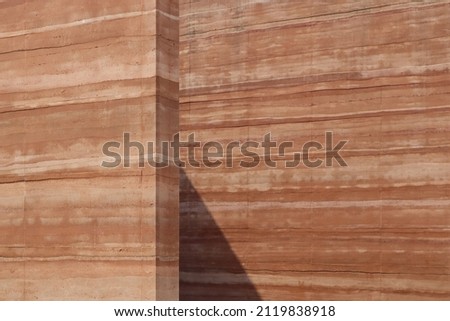 Rammed earth wall, clay old brown-orange background. Surface fine-grain grunge dirty. Natural raw materials mixed soil, gravel, sand, lime, or cement compacted stripe layers natural earth tones autumn