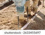 Rammer compacts soil as construction worker prepares ground at building site under work day
