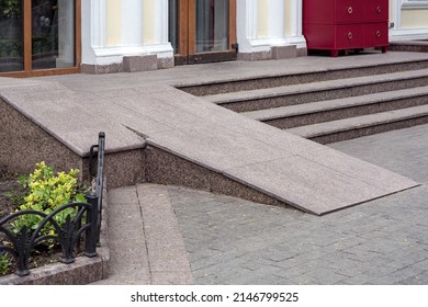 Ramped access, using wheelchair ramp for disabled people. Concrete ramp pathway near stone stairs of entrance to building side view, nobody.