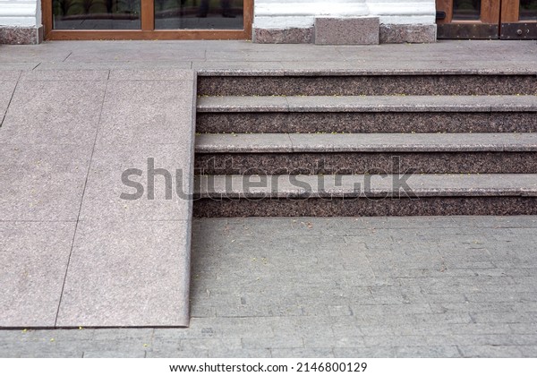 Ramped access, using\
wheelchair ramp for disabled people. Granite ramp pathway near\
stone tile stairs of entrance to cafe with glass door close-up\
front view, nobody.