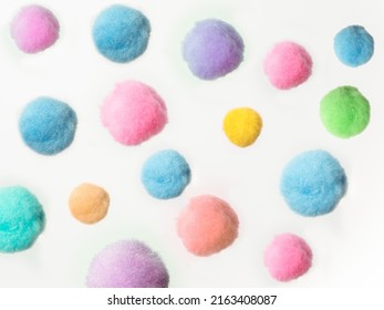 random arrangement of small fluffy pastel colored pom pom balls on a white background