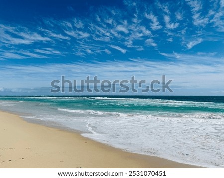 A random cloud display on show against a vivid blue sky above the crashing waves and foam washing up on the golden sands of west Australia at Yanchep Lagoon Bay.