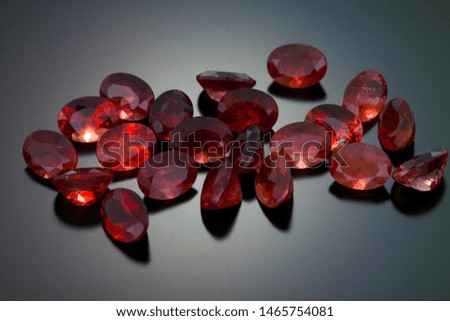 A random group of oval cut red orange colors sunstones sit on a black reflective background.